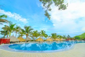 einen Pool mit Strohschirmen und Palmen in der Unterkunft Apartasuites Samaria - Club de Playa in Santa Marta