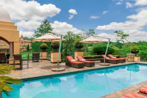 a swimming pool with patio furniture and umbrellas at Sheraton Pretoria Hotel in Pretoria