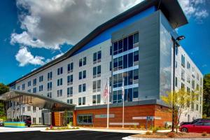 a large white building with a car parked in a parking lot at Aloft Raleigh Durham Airport Brier Creek in Raleigh