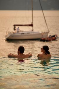 two people swimming in the water with a sail boat at Belfiore Park Hotel****S in Brenzone sul Garda