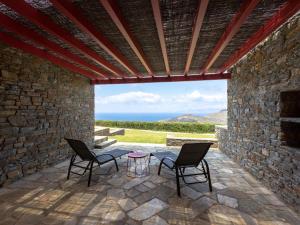 a patio with two chairs and a table in front of a stone wall at Bella Resorts Andros in Andros