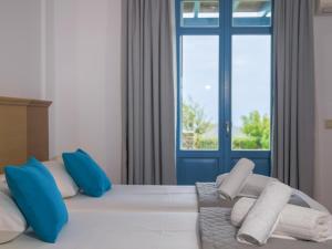 a bed with blue and white pillows and a window at Bella Resorts Andros in Andros