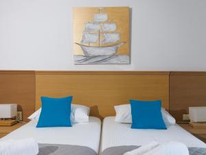 two beds with blue pillows and a painting of a ship at Bella Resorts Andros in Andros