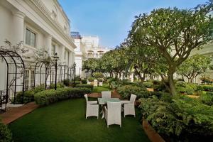 ITC Windsor, a Luxury Collection Hotel, Bengaluru في بانغالور: فناء به كراسي بيضاء وطاولة وأشجار