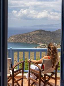 a woman sitting in a chair on a balcony looking at the ocean at Bella Resorts Andros in Andros