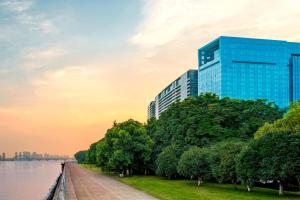 un bâtiment en verre à côté d'une rivière arborée dans l'établissement The Azure Qiantang, a Luxury Collection Hotel, Hangzhou, à Hangzhou