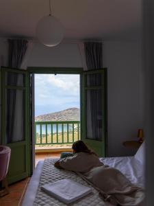 a woman laying on a bed in a bedroom with a window at Bella Resorts Andros in Andros