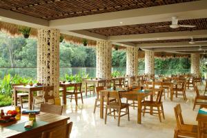 un restaurante con mesas y sillas de madera y ventanas en Sthala, A Tribute Portfolio Hotel, Ubud Bali en Ubud