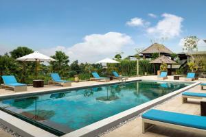 una piscina en un complejo con sillas y sombrillas azules en Sthala, A Tribute Portfolio Hotel, Ubud Bali, en Ubud