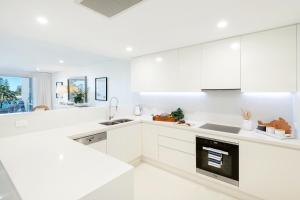 una cocina blanca con armarios blancos y fregadero en Kiama Waterfront Apartment en Kiama