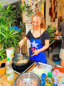 a woman cooking food in a pan on a stove at Back Home Backpackers in Bangkok