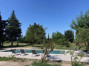 a swimming pool with three chairs and trees at Mas Du Petit Claux in Barbentane