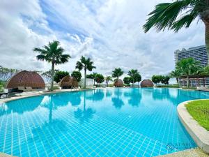 a large blue swimming pool with palm trees and huts at Almas Suites Puteri Harbour by Stayrene in Nusajaya
