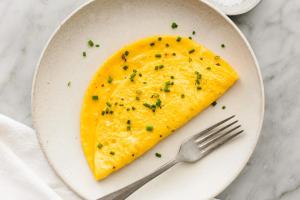 a white plate with a yellow omelet with chives on it at Yard Paradise Rooms Dhermi in Dhërmi