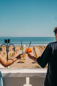 two people holding drinks on a beach with the ocean at Hotel Villa Sorriso in Lido di Jesolo