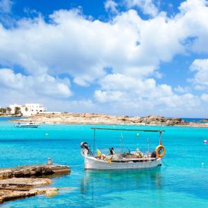 Mar Suites Formentera by Universal Beach Hotels في إس بوخولس: وجود قارب يجلس في الماء بالقرب من الشاطئ