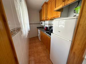La cuisine est équipée d'un réfrigérateur blanc et de placards en bois. dans l'établissement Apartamento Pascual, à Torrevieja