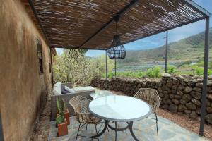 un patio con mesa, sillas y pared de piedra. en Casa rural cerca de la costa de La Laguna 2, en La Laguna