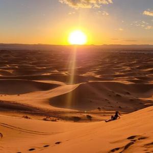 uma pessoa andando no deserto ao pôr do sol em Magic Luxury Camp em Merzouga