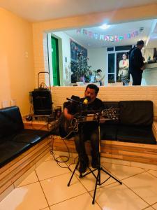 a man sitting on a couch with a guitar at Joshua Tree Hostel - Curitiba in Curitiba