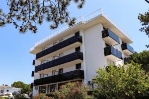 ein weißes Apartmenthaus mit Balkonen und Bäumen in der Unterkunft Hotel Eden in Lignano Sabbiadoro