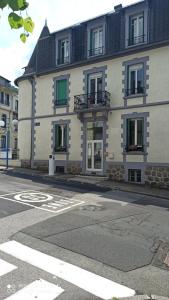 ein großes weißes Gebäude mit grünen Rollläden auf einer Straße in der Unterkunft La Tour Pom'Pin in La Bourboule