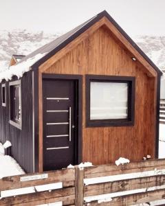 a wooden cabin with a black door in the snow at Patagonia Tiny House in El Chalten