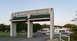 een bord dat zegt boeren rivierdorp op een parkeerplaats bij Brinkley's River Village in Klein-Brakrivier