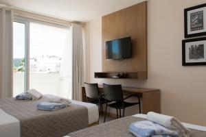 Habitación de hotel con 2 camas, escritorio y TV. en Belluno Apart Hotel en Florianópolis