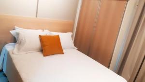 a bed with an orange pillow on top of it at Flat Asa Sul Condomínio Golden Place by CentoeDez in Brasilia