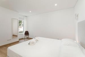 a white bedroom with a large bed and a chair at Centralgarve - Premium Apartment in the Center of Vilamoura - Cota10 in Vilamoura