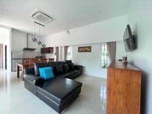 a living room with a black leather couch and a kitchen at 拉威查龙山顶大佛三卧泳池别墅Thaiya Villa in Ban Klang