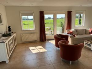 a living room with a couch and chairs and windows at Gastenverblijf WeijdeBlik in Sinderen