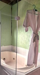 a bath tub with a shower curtain and a robe at Pousada Terraço Penedo in Penedo