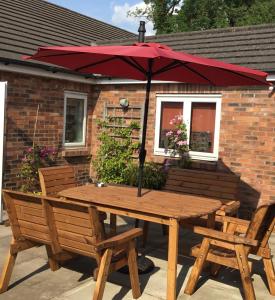 a wooden table and chairs with a red umbrella at Strawberry Fields in Cockermouth