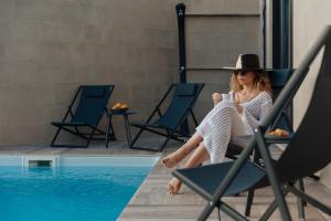 Aria di Mare Apartments في تيفات: وجود امرأة جالسة على كرسي بجانب مسبح