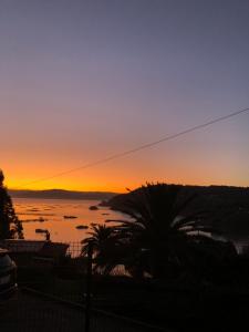 a sunset over a body of water with a palm tree at La Cabaña del tío Tom in Veigue