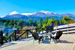 two people sitting on a deck with mountains in the background at Departamentos Tres Maitenes in Villa La Angostura