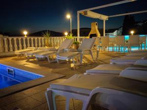 - une rangée de chaises longues à côté de la piscine la nuit dans l'établissement Apartments Ćurić, à Trogir
