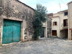 un bâtiment en briques avec une porte de garage verte et un arbre dans l'établissement Maison de village avec patio, à Bessan
