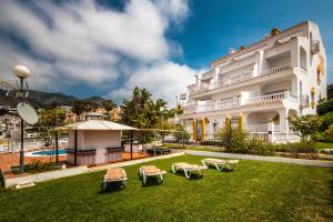 a large white building with a yard with benches at Apartamentos Las Rosas de Capistrano in Nerja