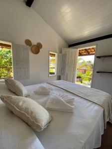 a large white bed with pillows and two windows at Pousada Amora Caraiva in Caraíva
