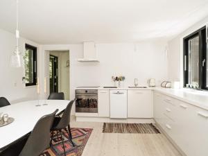 ティスヴィレライにあるHoliday home Tisvildeleje XVの白いキャビネット、テーブルと椅子付きのキッチンが備わります。