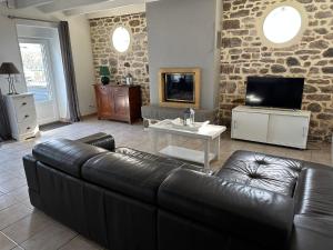 ein Wohnzimmer mit einem Ledersofa und einem TV in der Unterkunft La maison du chêne 3 in Miniac-Morvan