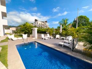 a swimming pool with white chairs and a house at Pura Vida Apartment with nice pool walking distance to the heart of Jaco in Jacó