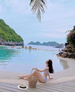 a woman in a bikini sitting on a beach at Nhật Anh Hotel Cát Bà in Cat Ba