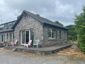 una casa de piedra con sillas rosas en el porche en Lakeland Midsummer Lakehouse en Oughterard