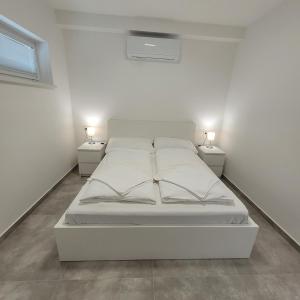 ein weißes Bett in einem weißen Zimmer mit zwei Lampen in der Unterkunft Szabadszél Apartmanok in Fonyód