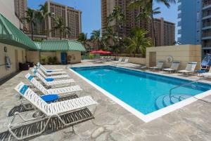 um grupo de espreguiçadeiras e uma piscina em Ramada Plaza by Wyndham Waikiki em Honolulu