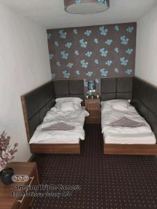 2 Einzelbetten in einem Zimmer mit blauen Blumen an der Wand in der Unterkunft Plage apartman in Hajdúszoboszló